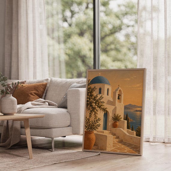 Santorini church wall art print leaning on the floor beside a cream armchair next to large garden windows.