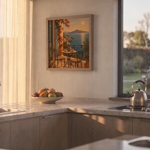 Mediterranean balcony wall art print hanging above a stone countertop with a fruit bowl in a sunny kitchen.