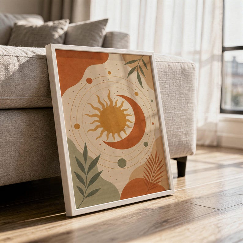 Celestial sun and moon art print in a white frame leaning against a gray sofa on a sunlit wooden floor.