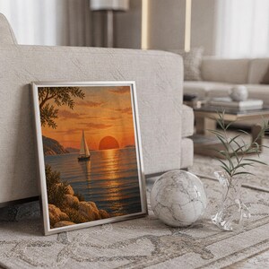 Sunset sailboat wall art print in a silver frame leaning against a sofa beside a decorative marble sphere.