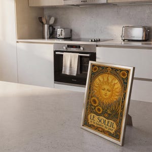 Art nouveau sunflower wall art print leaning on the floor beside a cream armchair next to large garden windows.