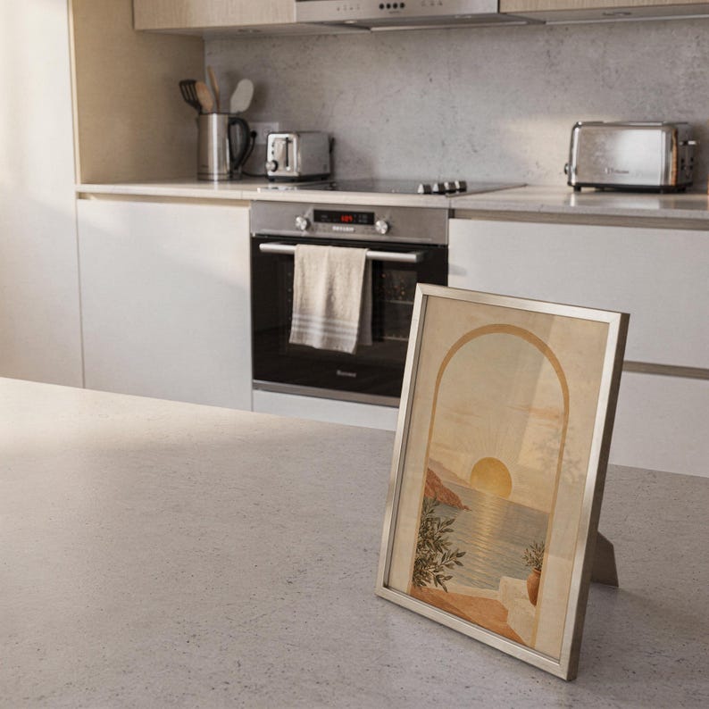 Mediterranean sunset arch print standing on a countertop in a modern white kitchen.