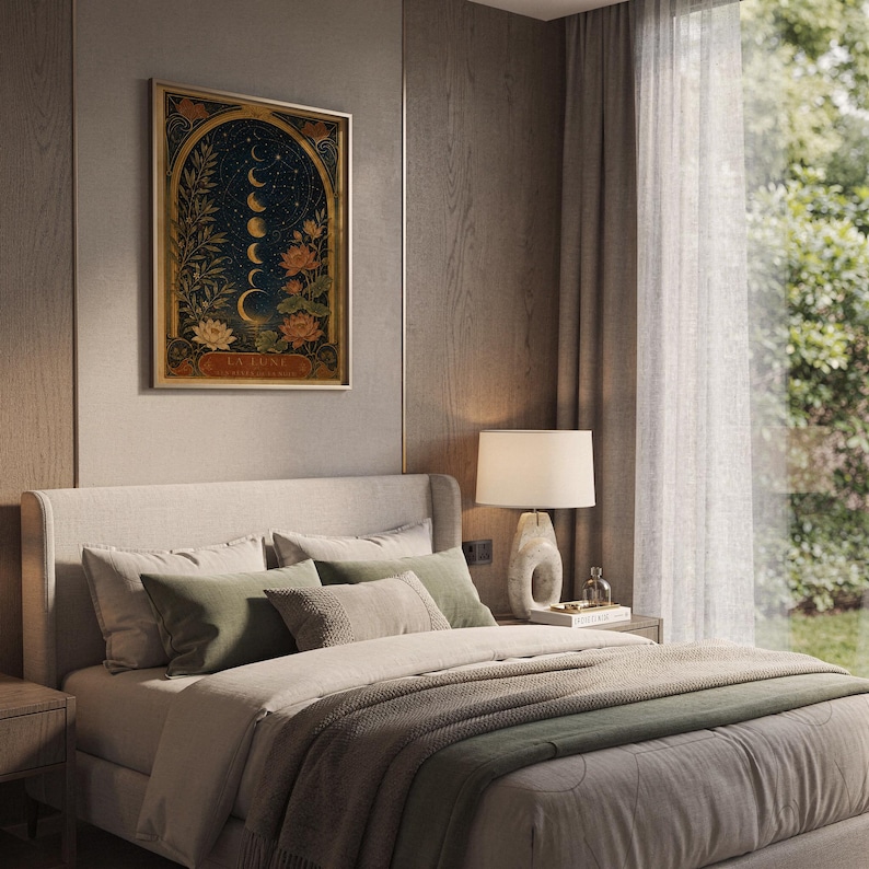 Moon phase wall art print hanging above a bed with sage green pillows in a calm neutral bedroom.