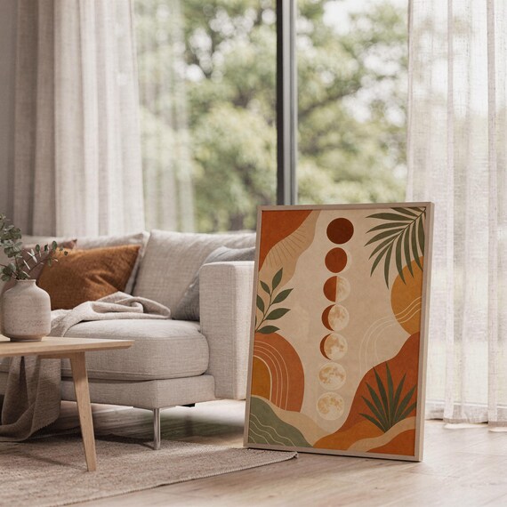 Boho moon phases art print leaning on the floor beside a cream armchair next to large garden windows.