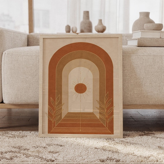 Boho arch sun wall art print featuring terracotta, warm tan, caramel brown, and cream tones with layered geometric arches, a radiant sun, and delicate botanical leaves, framed and leaning against a beige sofa on a textured rug in a bright Scandinavian living room.