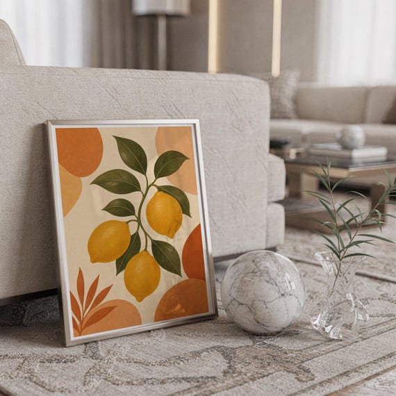 Lemon branch botanical print in a silver frame leaning against a sofa beside a decorative marble sphere.