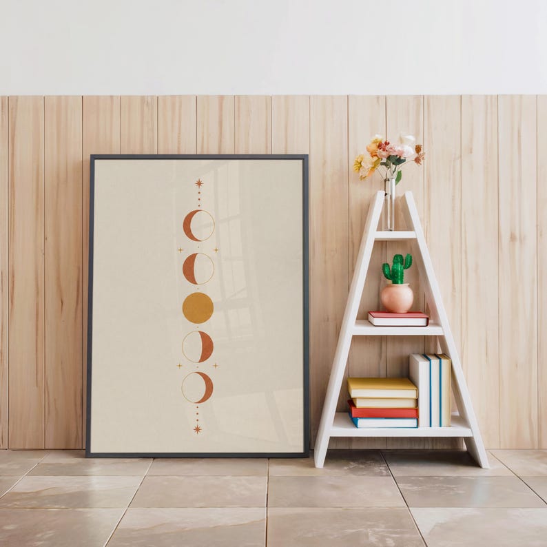 Spiritual moon phases poster in black frame beside white decorative ladder shelf