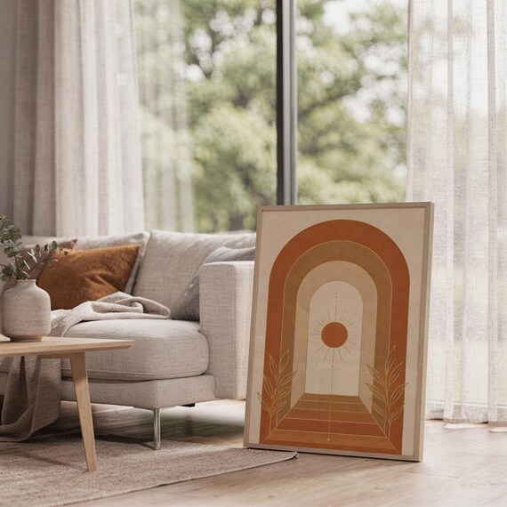 Boho arch sun wall art print leaning on the floor beside a cream armchair next to large garden windows.