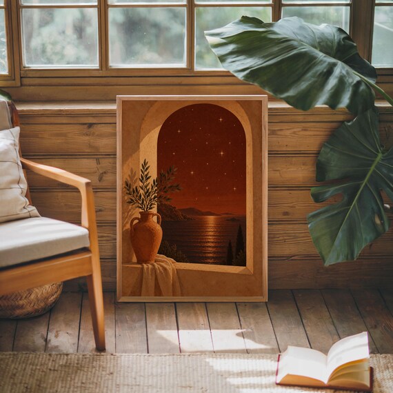 Mediterranean night sea wall art print leaning against warm wood paneling beside a wooden armchair and a monstera plant.