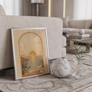 Mediterranean sunset arch print in a silver frame leaning against a sofa beside a decorative marble sphere.