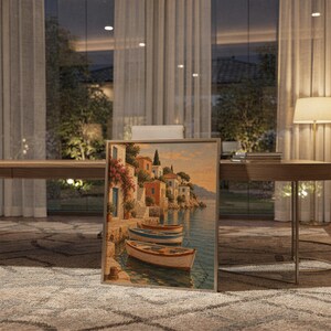Mediterranean coastal village wall art print standing on a wooden desk in a home office in warm evening light.