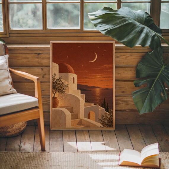 Mediterranean moonlit coastal wall art print leaning against warm wood paneling beside a wooden armchair and a monstera plant.