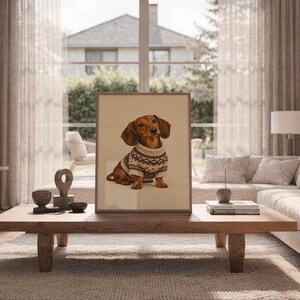 Dachshund sweater wall art print leaning on the floor beside a cream armchair next to large garden windows.