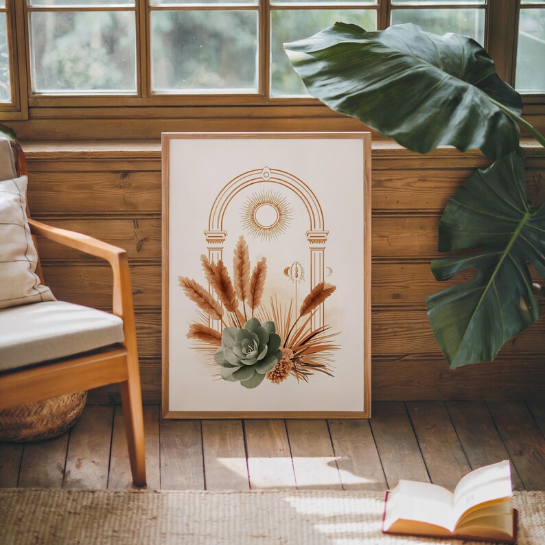 Celestial sun and pampas grass botanical poster framed on dark hardwood flooring near a sunlit window with large green monstera plant leaves, warm sunlight casting shadows on the wooden floor and wall in a cozy modern bohemian living room environment.