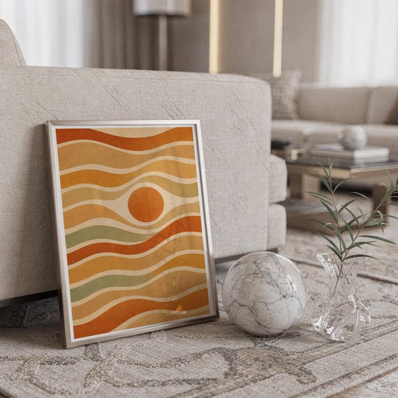 Abstract wavy sun print in a silver frame leaning against a sofa beside a decorative marble sphere.