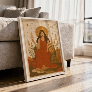 Celestial goddess wall art print in a white frame leaning against a gray sofa on a sunlit wooden floor.