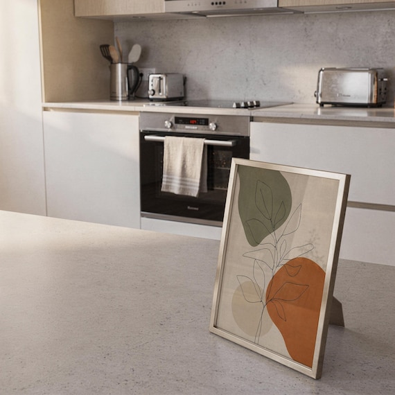 Small framed botanical line art piece leaning against the backsplash on a modern kitchen counter.