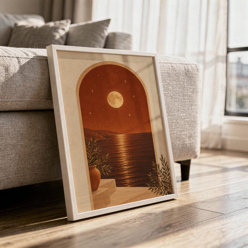 Moonlit Mediterranean arch print in a white frame leaning against a gray sofa on a sunlit wooden floor.