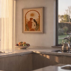 Framed romantic couple artwork resting on a kitchen countertop next to a fruit bowl with warm sunbeams streaming through the window.