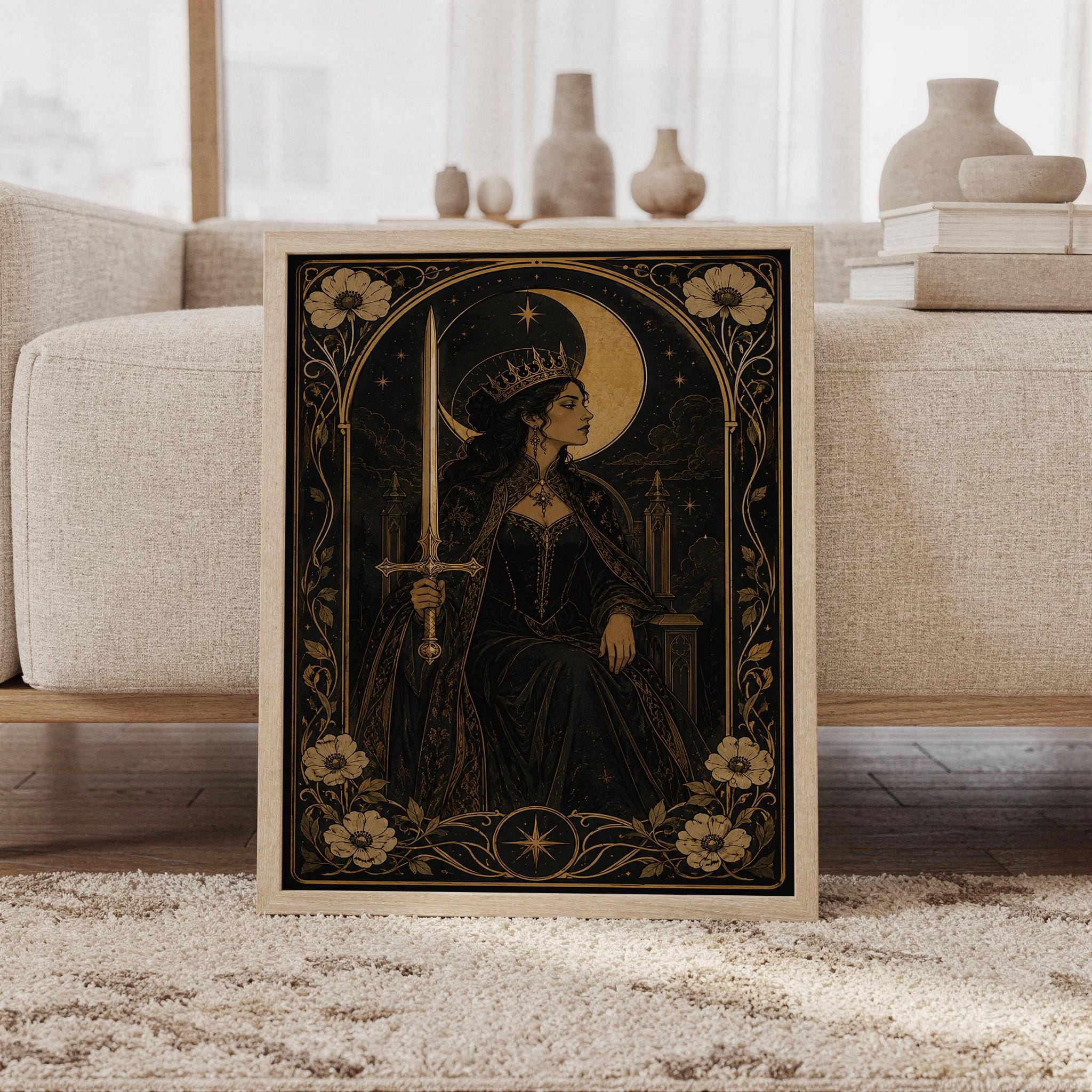 Gothic moon queen wall art print featuring antique gold, black, and warm sepia tones, a crowned warrior queen holding a sword before a glowing crescent moon, ornate florals, and stars, framed and leaning against a beige sofa on a textured rug in a bright Scandinavian living room.