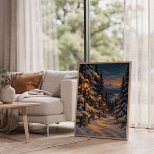 Snowy forest path wall art print leaning on the floor beside a cream armchair next to large garden windows.
