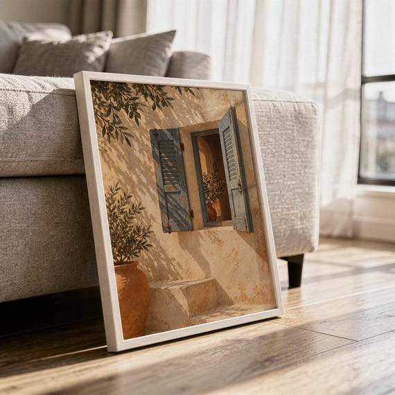 Mediterranean blue shutter wall art print in a white frame leaning against a gray sofa on a sunlit wooden floor.