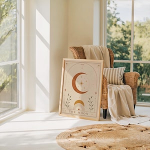 Single framed celestial art print leaning on a wooden floor near a sunlit window and armchair.
