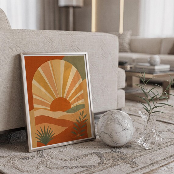 Boho sun arch print in a silver frame leaning against a sofa beside a decorative marble sphere.