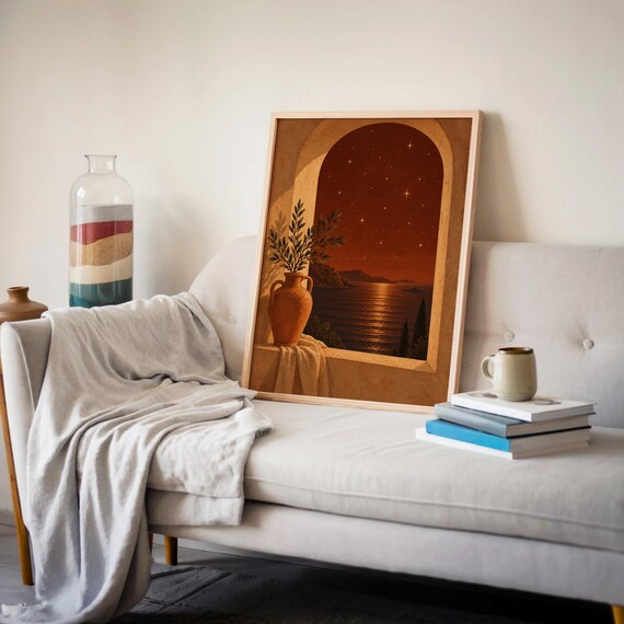 Mediterranean night sea wall art print leaning on a cream sofa against a beige wall beside books and a mug.
