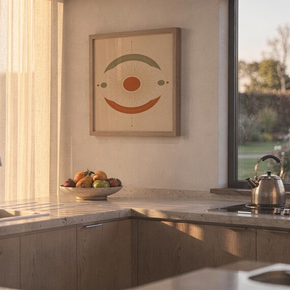 Abstract sun wall art print hanging above a stone countertop with a fruit bowl in a sunny kitchen.