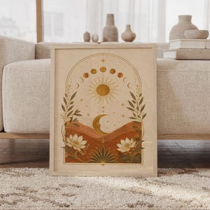 Celestial sun and moon wall art print featuring warm gold, terracotta, cream, and olive tones, moon phases, a radiant sun, crescent moon, stars, mountains, and botanical flowers in a vintage boho style, framed and leaning against a beige sofa on a textured rug in a bright Scandinavian living room.