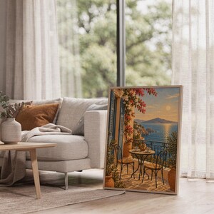 Mediterranean balcony wall art print leaning on the floor beside a cream armchair next to large garden windows.
