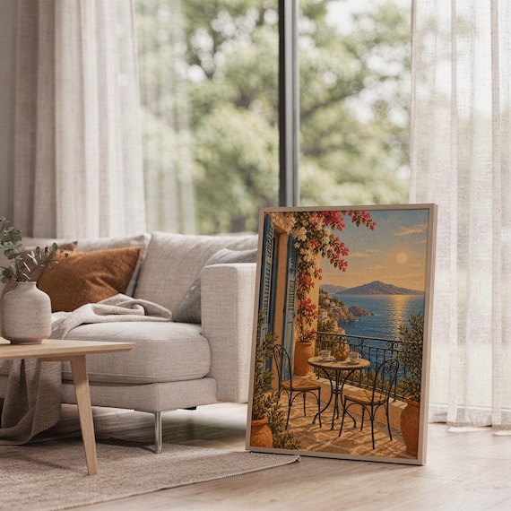 Mediterranean balcony wall art print leaning on the floor beside a cream armchair next to large garden windows.