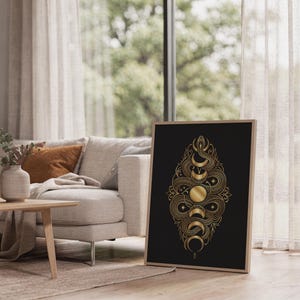 Gold snake moon phase wall art print leaning on the floor beside a cream armchair next to large garden windows.