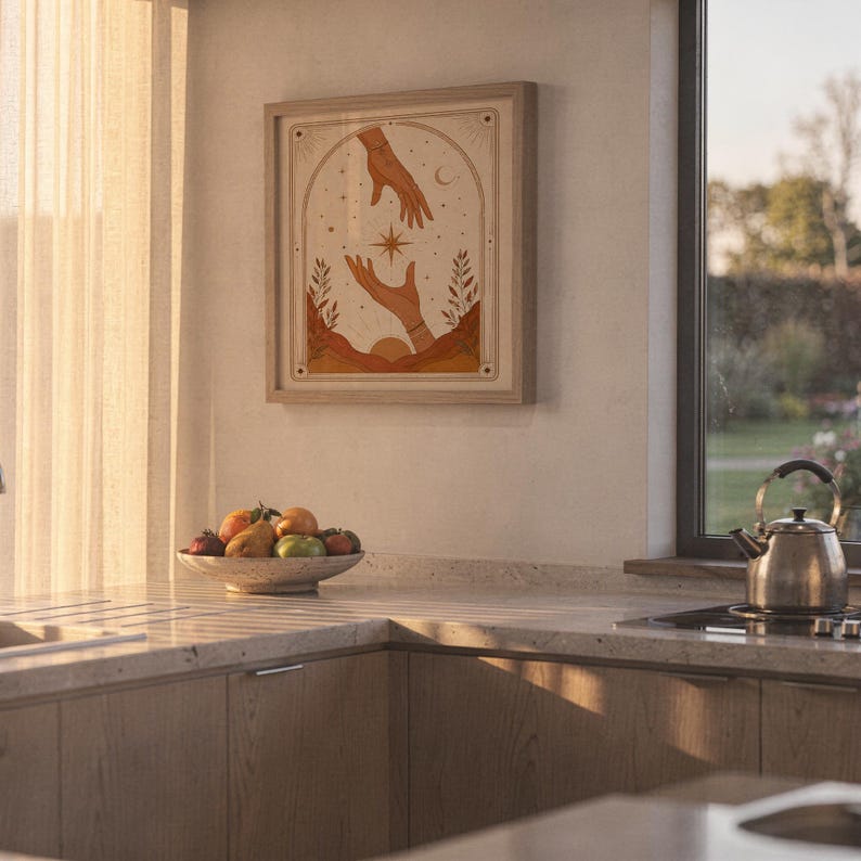 Earthy terracotta hands tarot print framed on kitchen wall illuminated by warm sunset light.