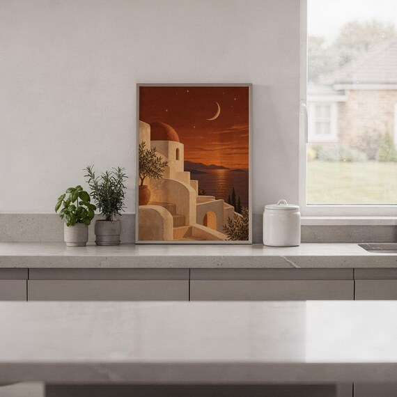 Mediterranean moonlit coastal wall art print standing on a white kitchen counter beside potted herbs.