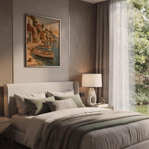 Mediterranean coastal village wall art print hanging above a bed with sage green pillows in a calm neutral bedroom.