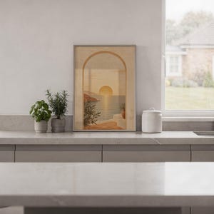 Mediterranean sunset arch print standing on a white kitchen counter beside potted herbs.