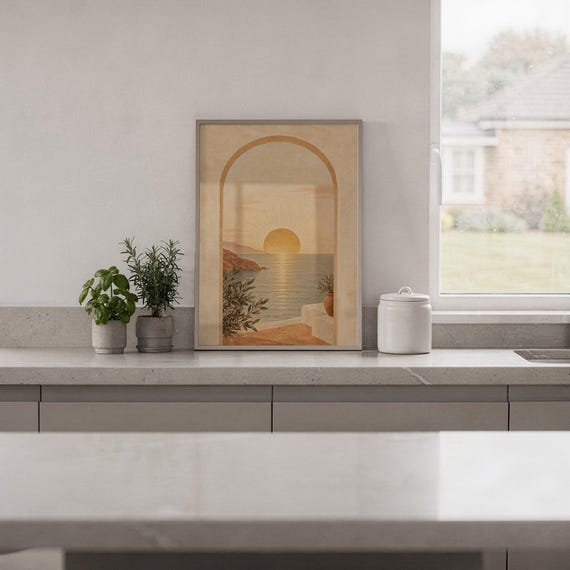 Mediterranean sunset arch print standing on a white kitchen counter beside potted herbs.