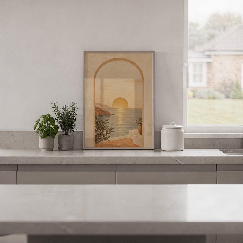 Mediterranean sunset arch print standing on a white kitchen counter beside potted herbs.