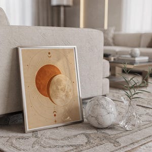 Sun and moon celestial wall art print in a silver frame leaning against a sofa beside a decorative marble sphere.