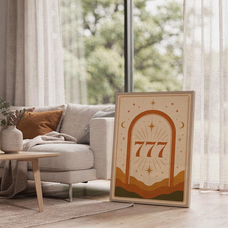 Framed neutral 777 celestial art print leaning on the carpet next to a light wood coffee table and cozy living room sofa.