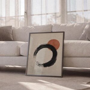 Black framed abstract circle art piece resting on the floor beside a white sofa.