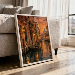 Venice canal sunset wall art print in a white frame leaning against a gray sofa on a sunlit wooden floor.