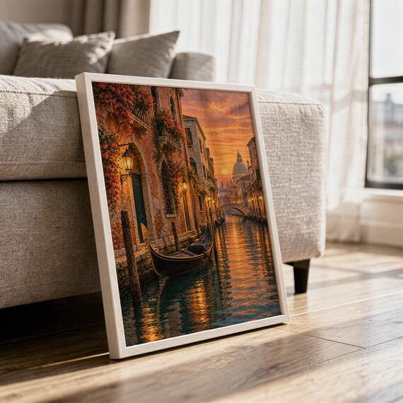 Venice canal sunset wall art print in a white frame leaning against a gray sofa on a sunlit wooden floor.