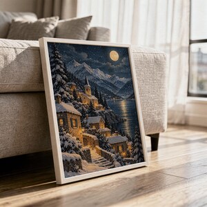 Snowy mountain village wall art print in a white frame leaning against a gray sofa on a sunlit wooden floor.