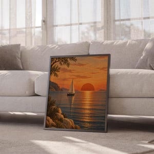 Sunset sailboat wall art print leaning against a white sofa in a bright living room with sheer curtains.