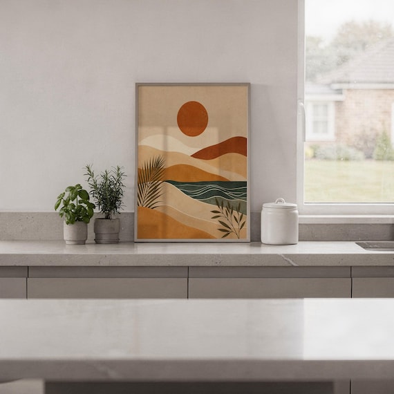 Muted modern abstract landscape art framed on kitchen wall above wooden cabinets in home.