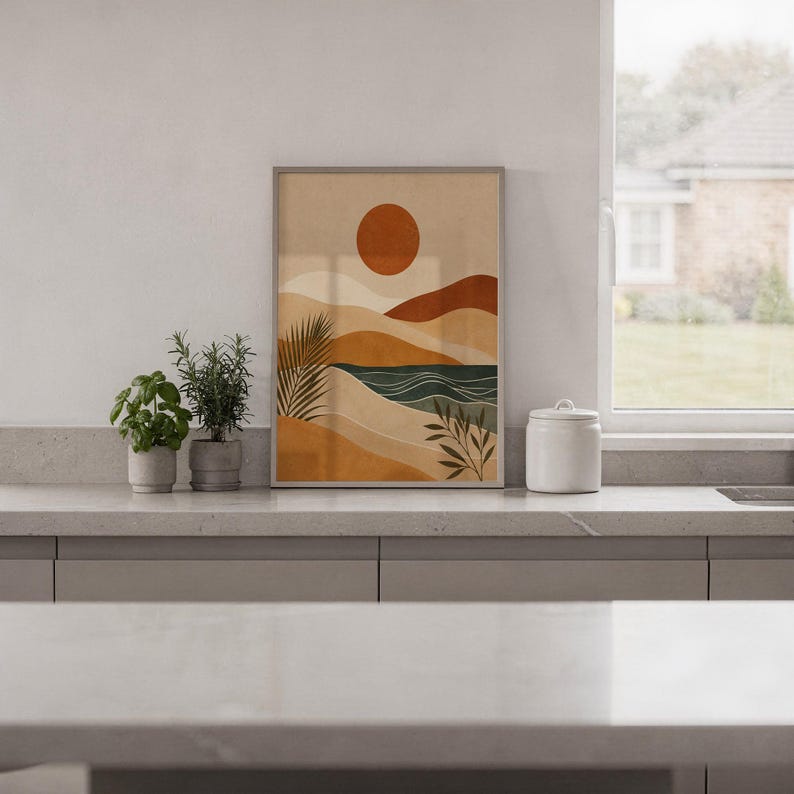 Muted modern abstract landscape art framed on kitchen wall above wooden cabinets in home.