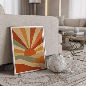 Retro geometric sunrise print in a silver frame leaning against a sofa beside a decorative marble sphere.